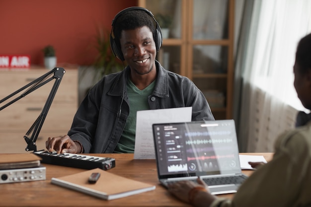 Retrato de joven afroamericano sonriendo felizmente mientras compone música en casa con pareja