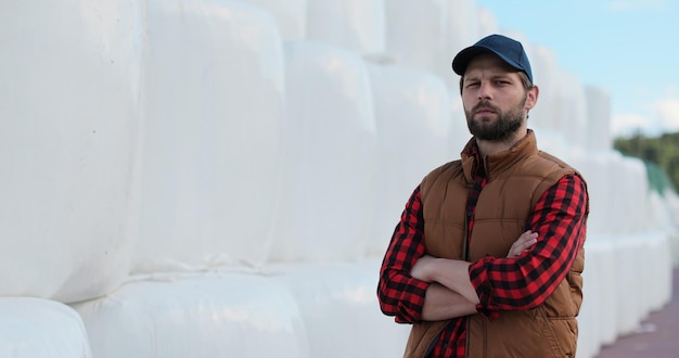 Retrato de un joven agricultor guapo con camisa y chaleco naranja mirando a la cámara en el fondo de la pila de heno Agronegocios orgánicos modernos