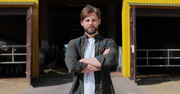 Retrato de un joven agricultor guapo en camisa mirando a la cámara en el fondo de la granja lechera Concepto de cría de la industria agrícola