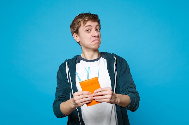 Retrato de joven alegre asombrado en ropa casual con pasaporte, boleto de embarque aislado en la pared azul. Personas sinceras emociones, concepto de estilo de vida.