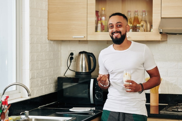 Retrato de joven alegre comiendo yogur no lácteo para el desayuno cuando está de pie en la cocina