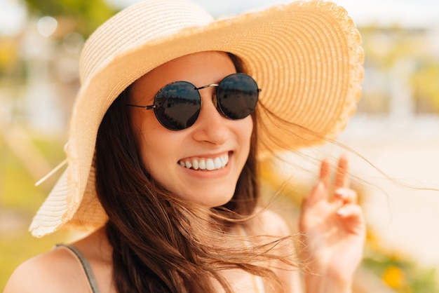Retrato de una joven alegre con gafas de sol y un sombrero para el sol de cerca.