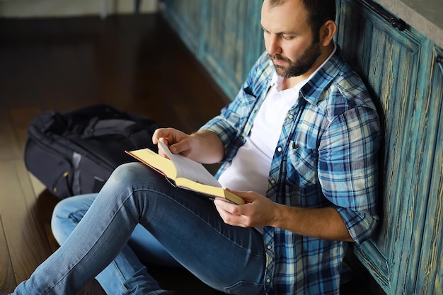 Retrato de un joven alegre leyendo un libro mientras se sienta en el piso de su sala de estar. Estudiante sosteniendo y leyendo un libro.