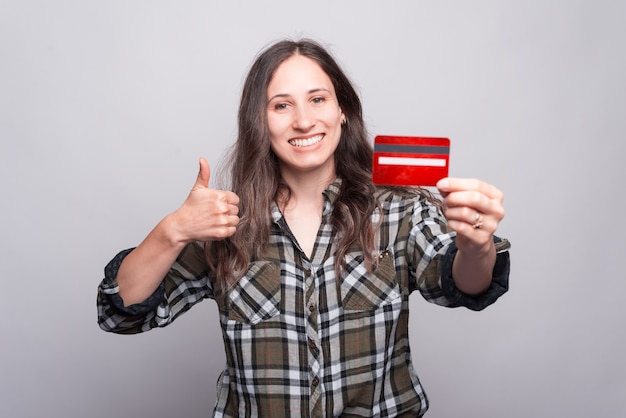 Foto retrato de joven alegre mostrando el pulgar hacia arriba y sosteniendo la tarjeta de crédito roja. feliz de comprar en línea