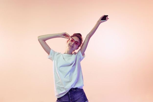 Retrato de una joven alegre posando con ropa informal Camiseta y jeans aislados sobre fondo de estudio rosa con luz de neón