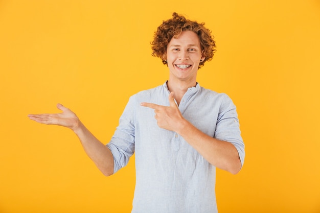 Retrato de joven alegre publicidad y sosteniendo copyspace en la mano, aislado sobre fondo amarillo