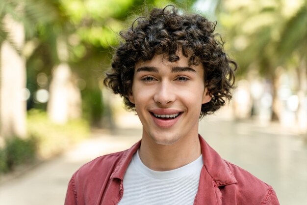 Retrato de un joven alegre y rizado parado en el parque de la ciudad en un día cálido y soleado y sonriendo