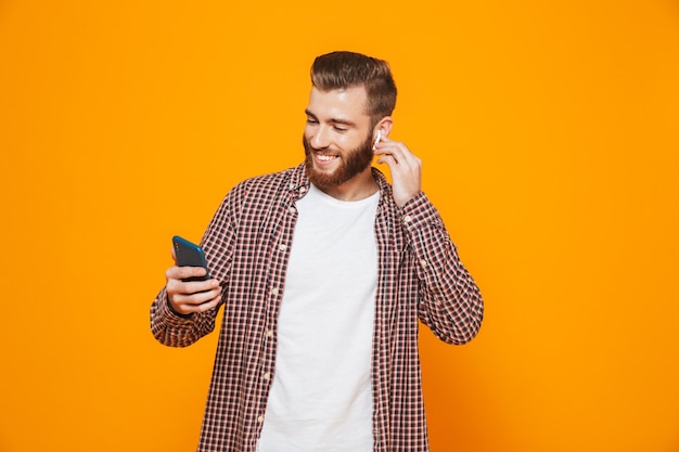 Retrato de un joven alegre con ropa casual escuchando música con auriculares y teléfono móvil