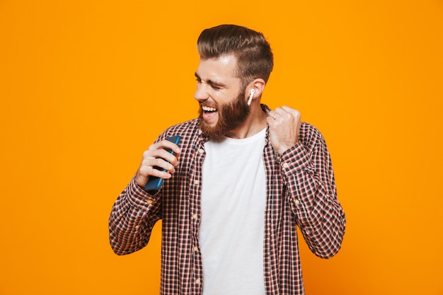 Retrato de un joven alegre con ropa casual escuchando música con auriculares y teléfono móvil