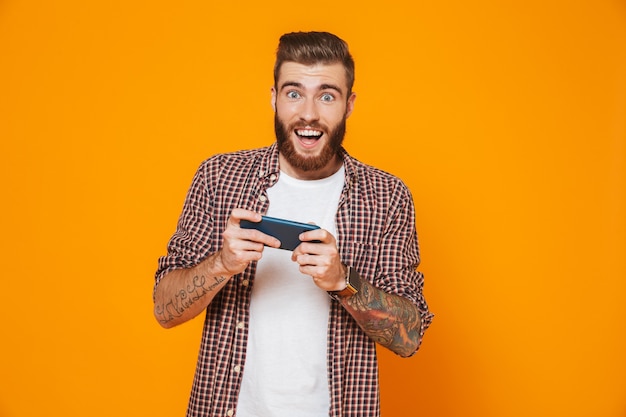 Retrato de un joven alegre con ropa casual jugando en el teléfono móvil