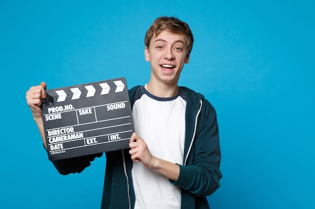 Retrato de joven alegre en ropa casual mantenga claqueta de cine negro clásico aislado en la pared azul. Personas sinceras emociones, concepto de estilo de vida.