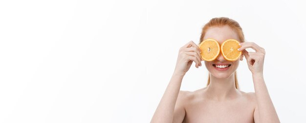 Retrato de una joven alegre sosteniendo dos rodajas de naranja en su cara sobre la pared blanca backgr