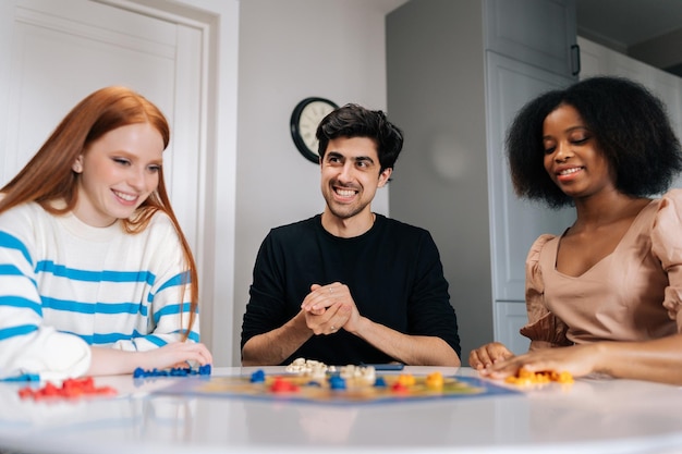 Retrato de un joven alegre tirando dados jugando en un juego de mesa con amigos multiétnicos disfrutando de actividades de ocio en casa