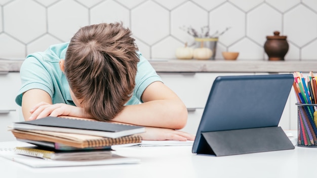 Retrato de un joven alumno cansado preadolescente acostado durmiendo con las manos dobladas en el escritorio cerca de la tableta de gafas de cuadernos en casa