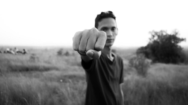 Foto retrato de un joven apretando el puño en un campo de hierba contra el cielo