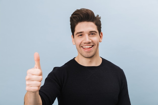 Foto retrato de un joven apuesto alegre que se encuentran aisladas en azul, dando pulgar hacia arriba