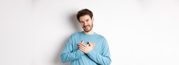 Retrato de un joven apuesto con barba cogido de la mano en el corazón y diciendo gracias pensando en