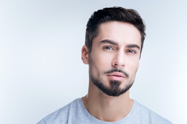 Retrato de un joven apuesto en camiseta gris posando contra la pared blanca