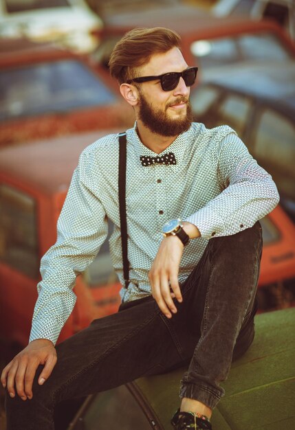 Retrato de un joven apuesto y elegante con camisa y pajarita con autos viejos