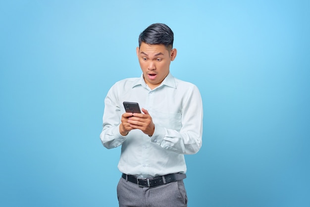 Retrato de un joven apuesto empresario sorprendido con smartphone sobre fondo azul.