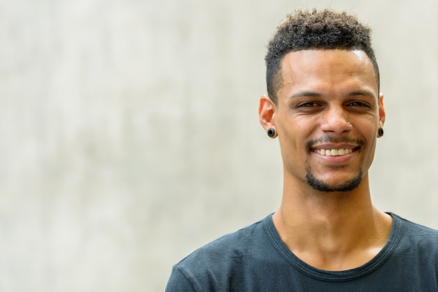 Retrato de joven apuesto hombre africano barbudo contra el muro de hormigón al aire libre