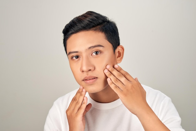 Retrato de joven apuesto hombre asiático sin camisa comprobando su rostro en busca de conceptos de belleza y cuidado de la piel