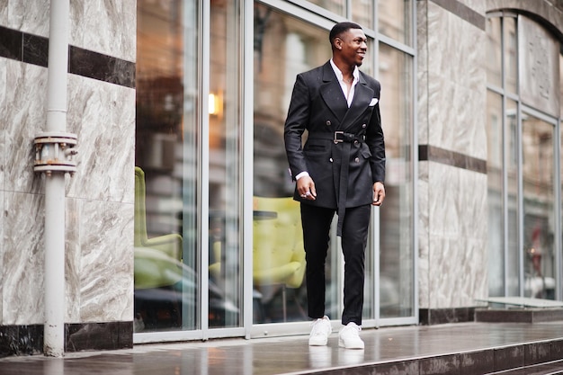 Retrato de joven y apuesto hombre de negocios afroamericano con traje y zapatillas blancas