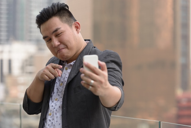 Retrato de joven apuesto hombre de negocios filipino con sobrepeso en traje contra la vista de la ciudad