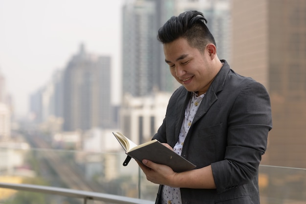 Retrato de joven apuesto hombre de negocios filipino con sobrepeso en traje contra la vista de la ciudad