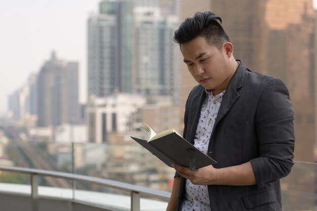 Retrato de joven apuesto hombre de negocios filipino con sobrepeso en traje contra la vista de la ciudad