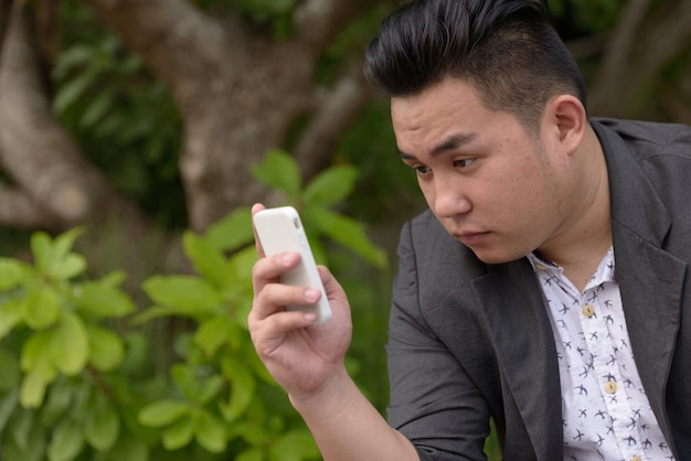 Retrato de joven apuesto hombre de negocios filipino con sobrepeso en traje relajante en el parque al aire libre