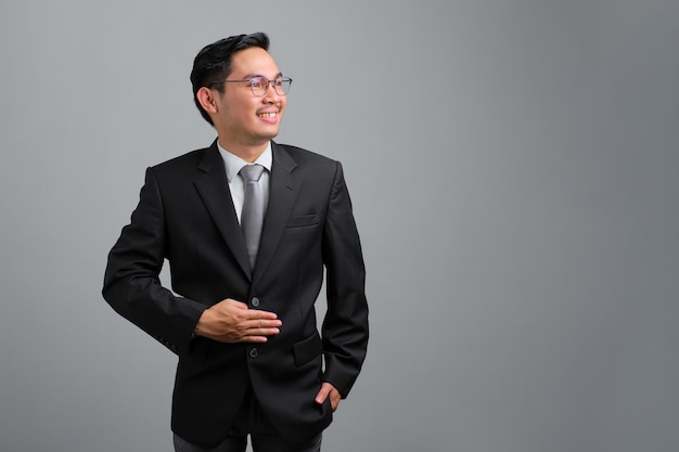 Retrato de un joven y apuesto hombre de negocios sonriente con traje formal que mira hacia otro lado y se siente confiado aislado en un fondo gris