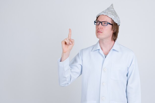 Retrato de joven apuesto médico con sombrero de papel de aluminio como concepto de teoría de la conspiración en blanco