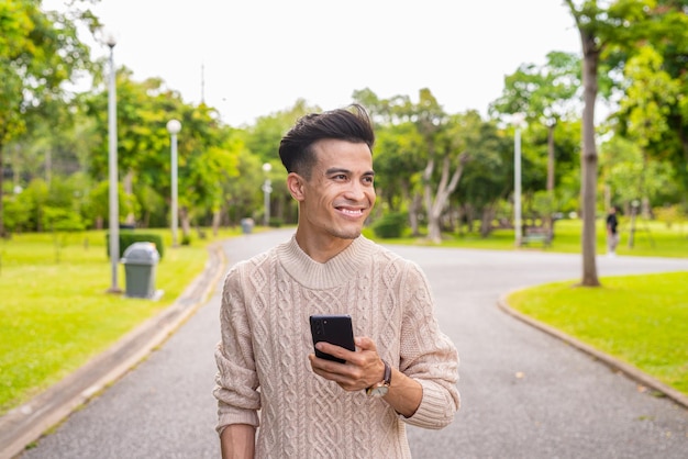 Retrato de un joven apuesto en el parque durante el verano usando el teléfono