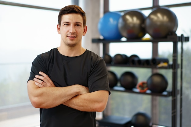 Retrato de un joven apuesto preparador físico en un gimnasio