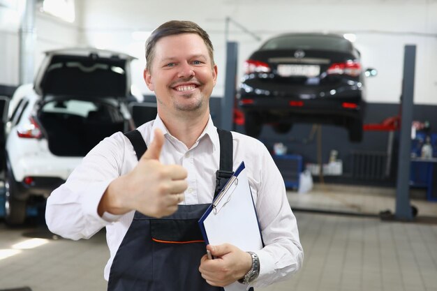 Retrato de un joven apuesto en uniforme con los pulgares hacia arriba en el fondo del servicio de automóviles