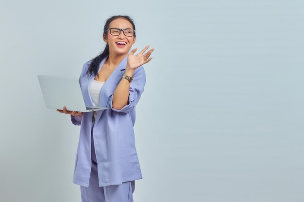 Retrato de una joven asiática alegre usando una laptop y gesticulando con la mano aislada de fondo blanco