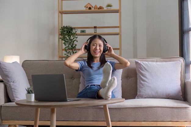 Retrato de una joven asiática feliz escuchando música con auriculares inalámbricos de una aplicación de música en una computadora portátil
