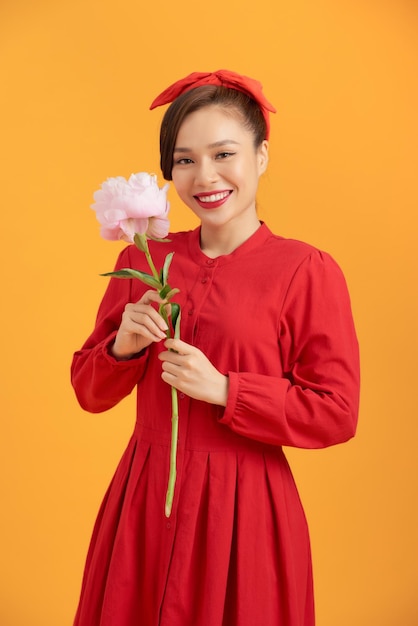 Retrato de una joven asiática feliz sosteniendo una flor de peonía sobre un fondo naranja