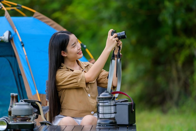 Retrato de una joven asiática feliz tomando una foto mientras se sienta en una silla en el camping