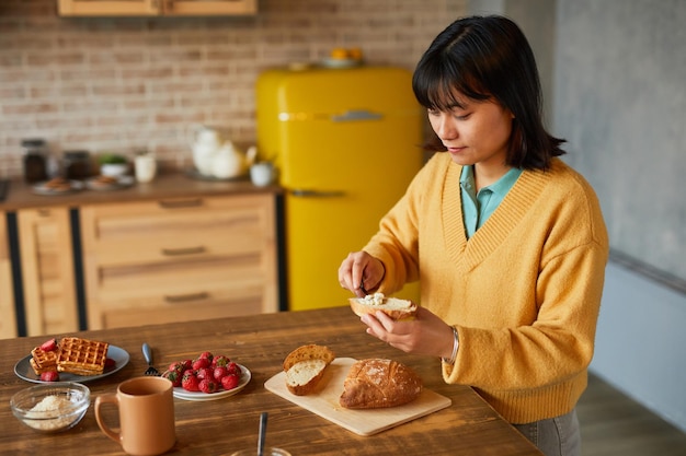 Retrato de una joven asiática haciendo un sándwich de queso mientras disfruta del desayuno en el espacio de copia de la cocina