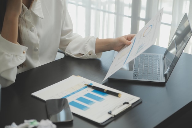 Retrato de una joven asiática independiente está trabajando en su trabajo en una tableta de computadora en una oficina moderna. Haciendo un informe de análisis contable. Datos de inversión inmobiliaria. Concepto de sistemas financieros y fiscales.