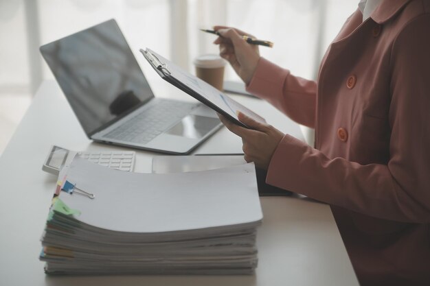 Retrato de una joven asiática independiente está trabajando en su trabajo en una tableta de computadora en una oficina moderna. Haciendo un informe de análisis contable. Datos de inversión inmobiliaria. Concepto de sistemas financieros y fiscales.