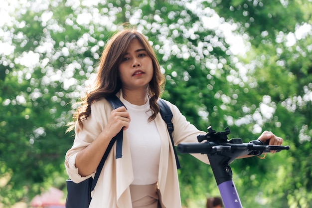 Retrato de una joven asiática montando scooter eléctrico en el parque