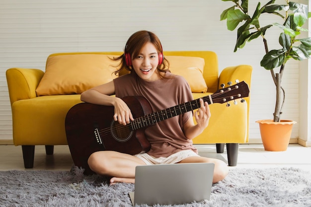 Foto retrato joven asiática pasando su tiempo libre tocando guitarra acústica en la sala de estar