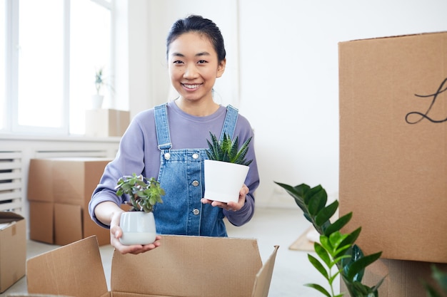 Retrato de joven asiática plantas de embalaje a cajas de cartón que se trasladan a una nueva casa o apartamento