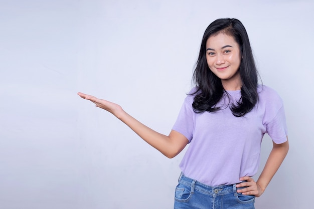 Retrato de joven asiática sonriendo con expresión alegre, muestra algo sorprendente en el espacio en blanco en un paño casual aislado sobre la pared