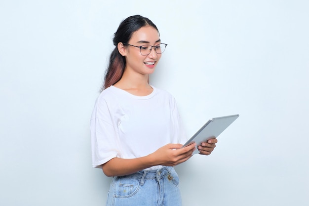 Retrato de una joven asiática sonriente con una camiseta blanca usando una tableta digital aislada de fondo blanco