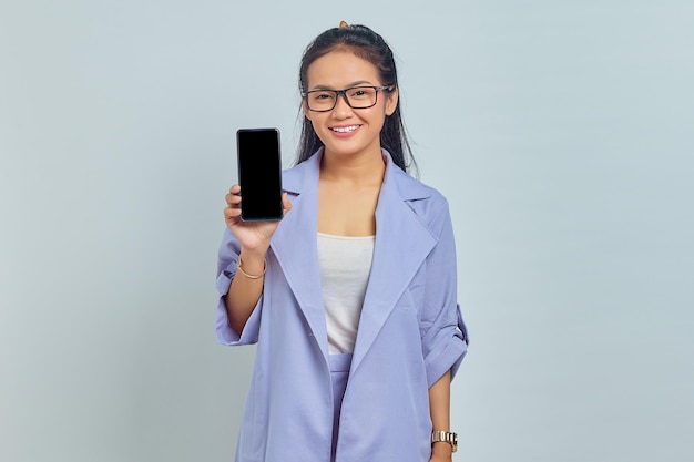 Retrato de una joven asiática sonriente que muestra un teléfono móvil con pantalla en blanco aislado de fondo blanco