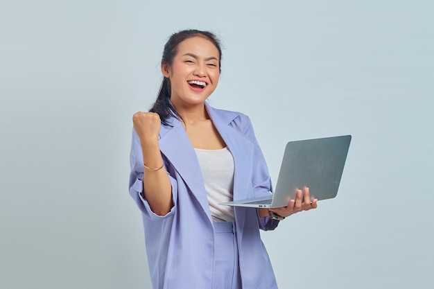 Foto retrato de una joven asiática sonriente sosteniendo un portátil y celebrando el éxito aislado de fondo blanco